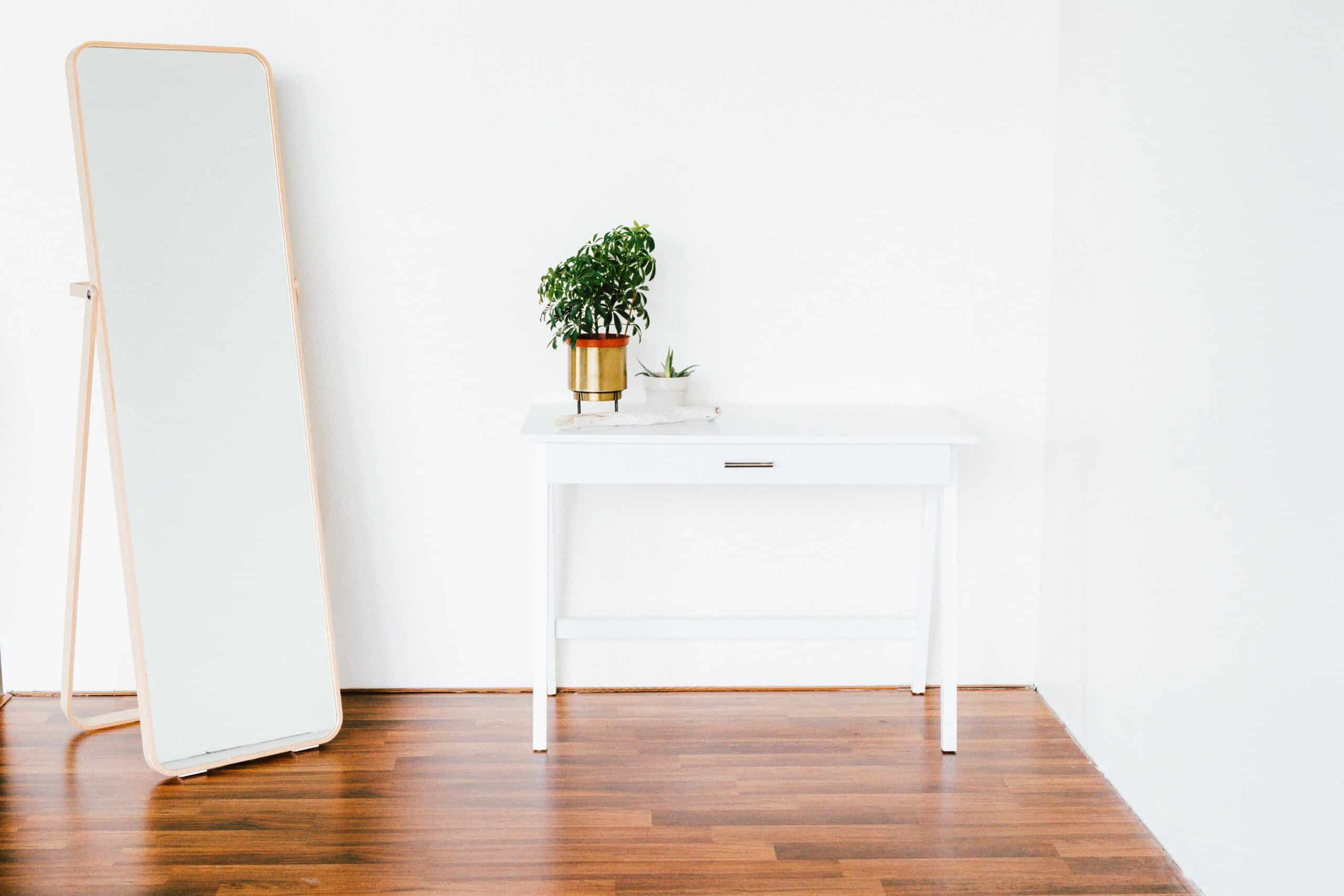A small desk and tall mirror sitting on restored wooden floors.